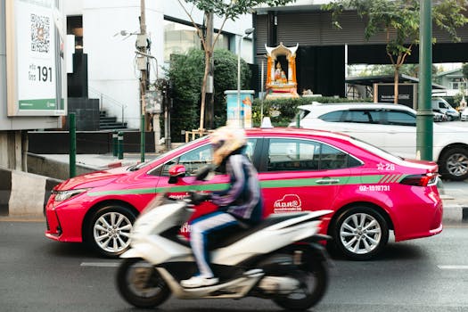 Dynamic urban scene featuring a motor scooter and pink taxi on a busy city street.
