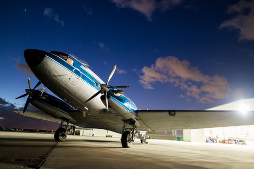Free A classic propeller airplane on a runway at twilight with colorful clouds and hangar in the background. Stock Photo