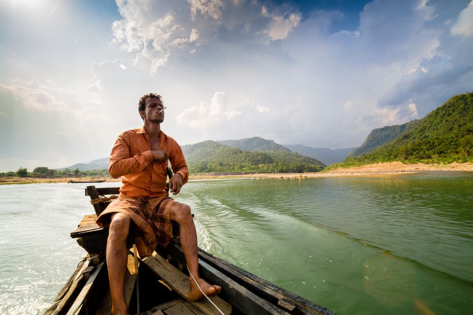 A man in a boat navigating a serene lake surrounded by lush green hills under a dramatic sky.