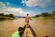 两名男子驾着一艘木船，行驶在一条宁静的河上，四周是郁郁葱葱的乡村