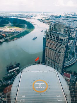 从无人机视角俯瞰现代城市景观，建筑物的屋顶直升机停机坪下是蜿蜒的河流