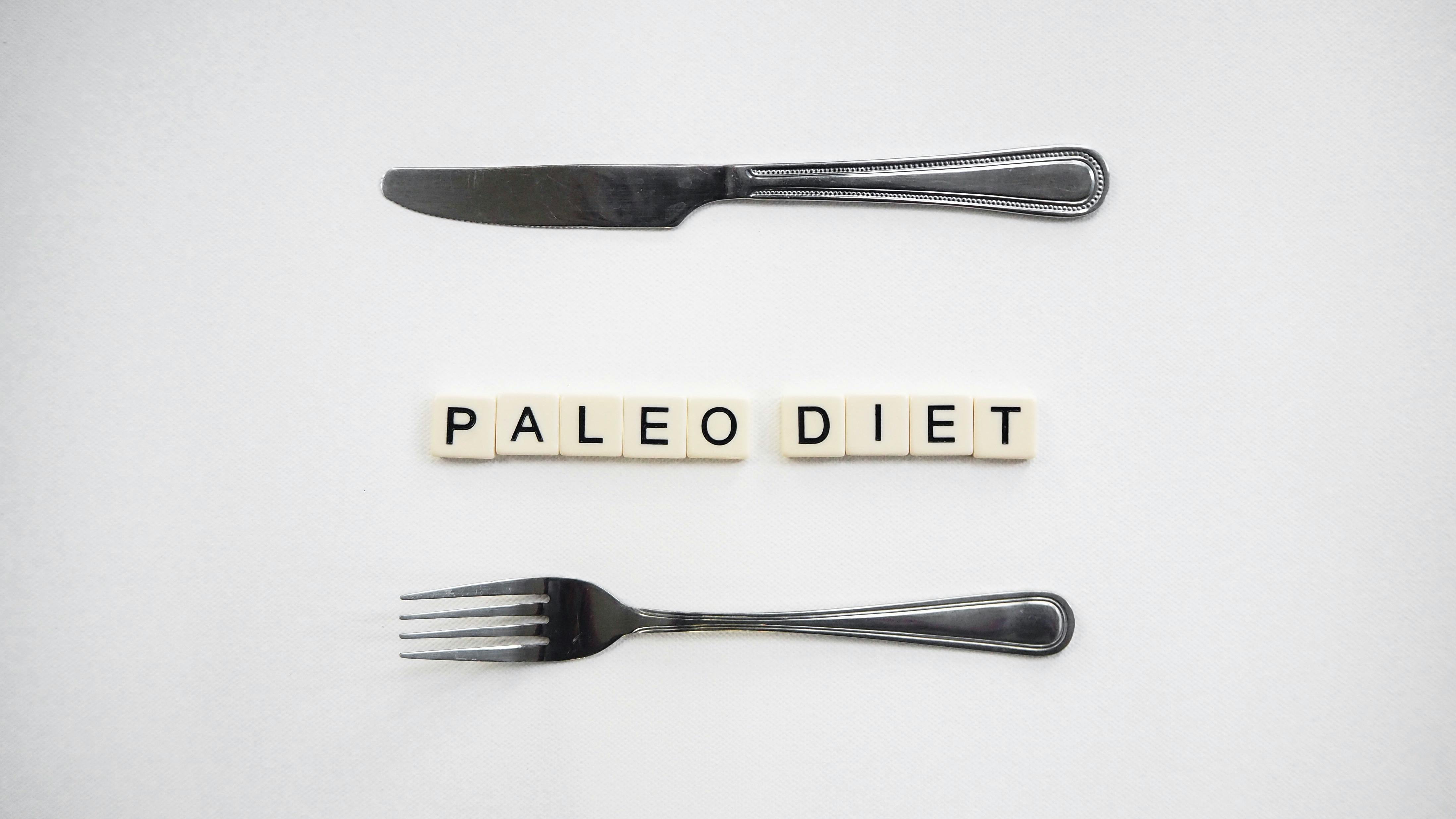 Flat lay of paleo diet concept with utensils and scrabble tiles on a white background.