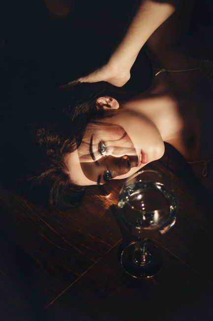 Elegant portrait of a young woman lying beside a wine glass, creating a dreamy and artistic composition.