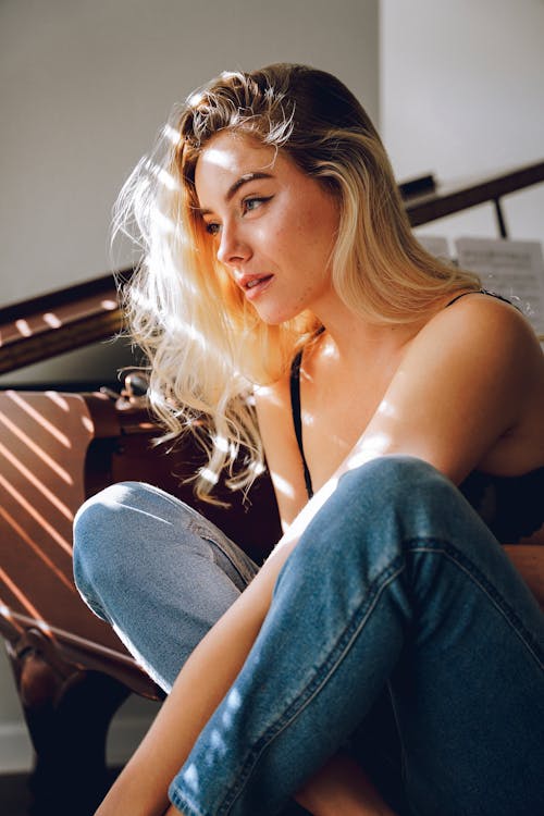 A beautiful blonde woman sitting on the floor near a piano