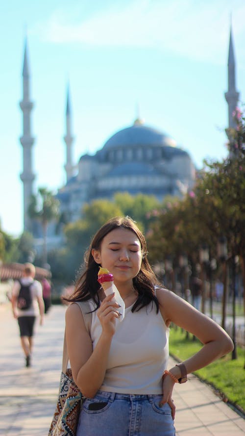 A woman is holding an ice cream in front of a mosque