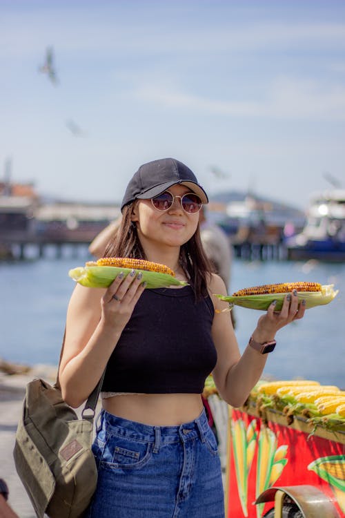 A woman holding two corn on the cob in front of the water