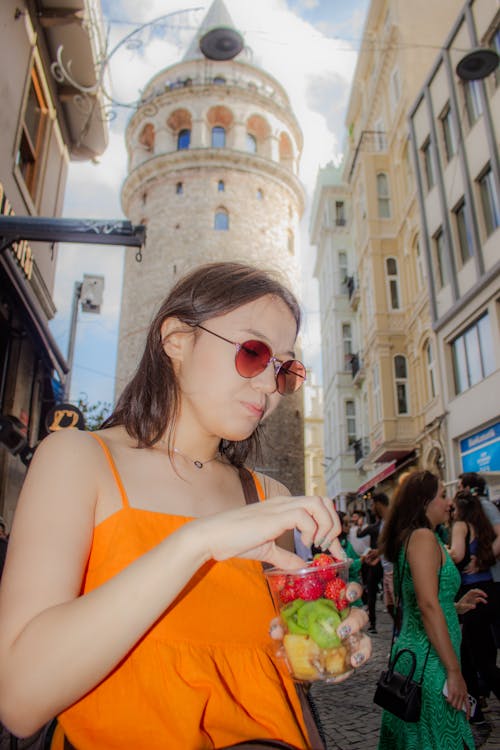 A woman in an orange dress is eating a fruit