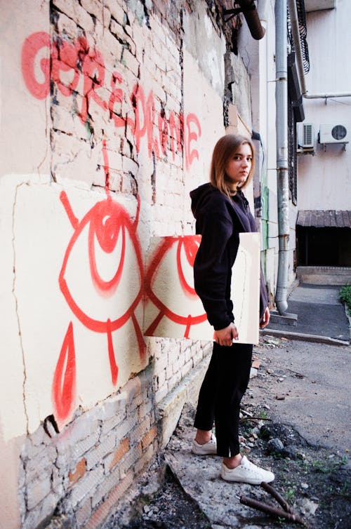 Foto De Una Mujer Con Una Sudadera Con Capucha Y Pantalones Negros De Pie Junto A La Pared