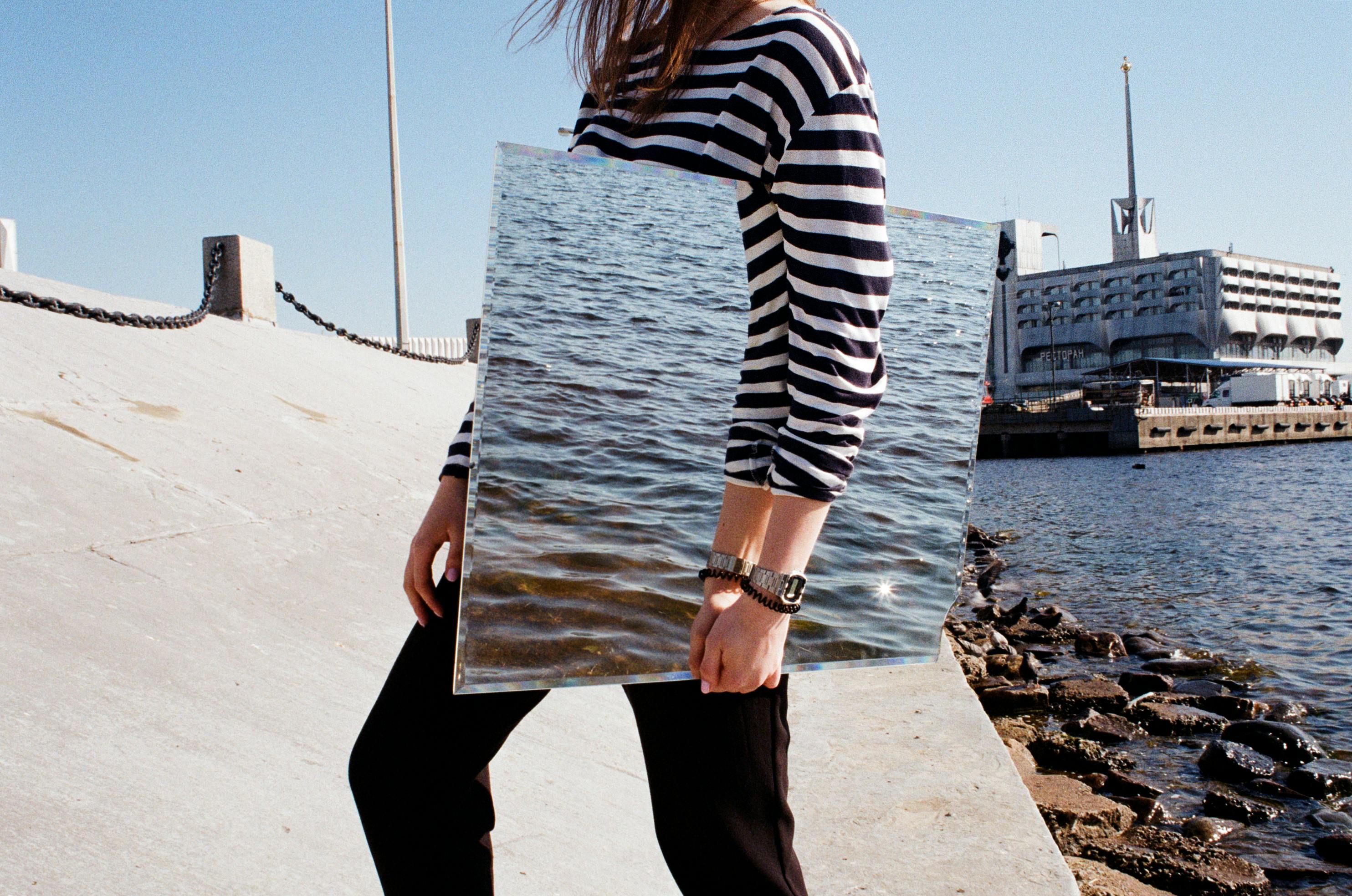 女人通过镜子反射大海，在城市滨水区营造出独特的水景效果