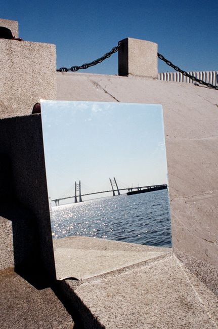 Artistic shot highlighting a bridge reflection in a mirror by the ocean under clear skies.