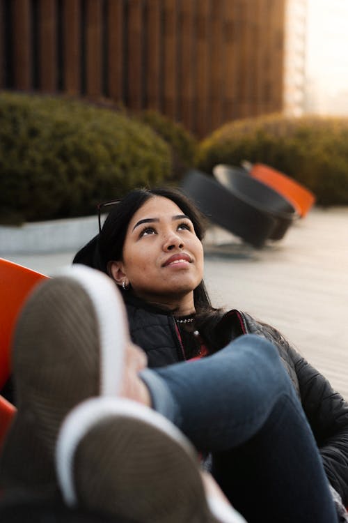 Free Photo of Woman in Black Jacket and Blue Denim Jeans Lying on Chair While Looking Up Stock Photo
