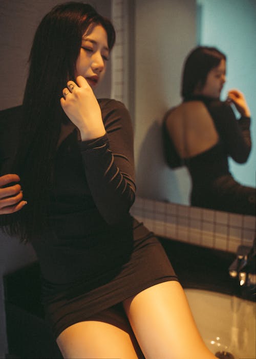 A woman in a black dress sitting on a sink