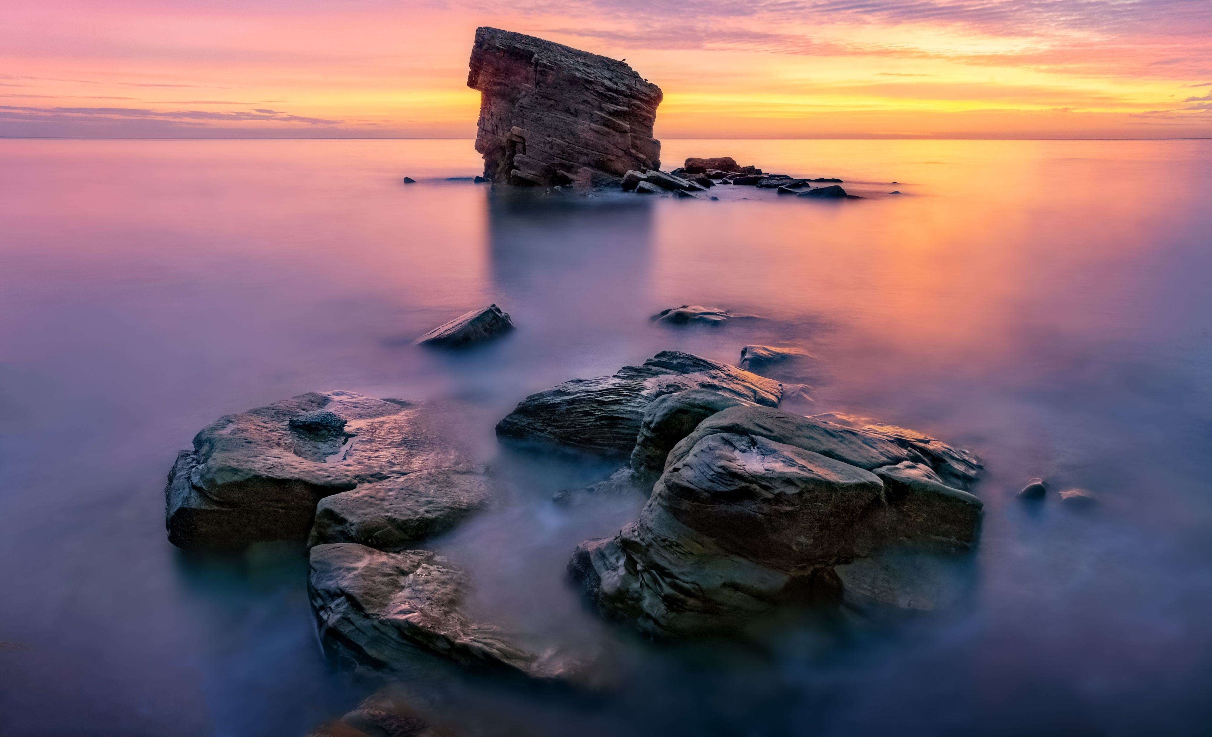 A rock in the ocean at sunset with purple sky · Free Stock Photo