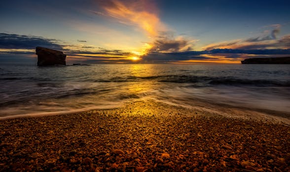 A stunning sunset illuminates a rocky beach with golden light, creating a scenic and serene seashore landscape.
