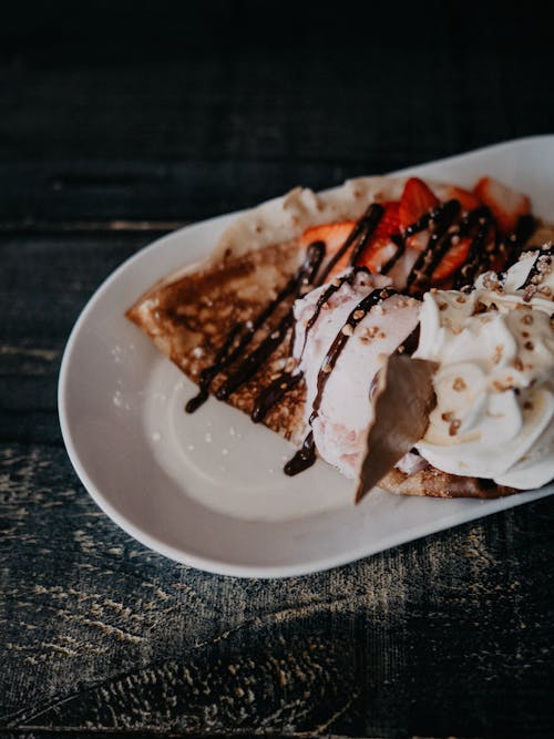 A white plate topped with a crepe and strawberries