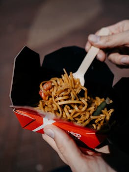 Street food noodle dish held in hands outdoors, showcasing vibrant flavors.
