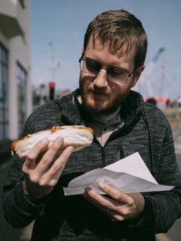 A man enjoys a delicious hot dog on a bustling city street, capturing the essence of street food culture.
