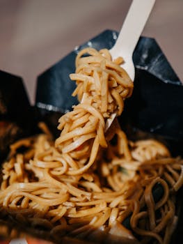 Close-up shot of delicious Asian noodles in takeout box with sunlight highlighting texture.