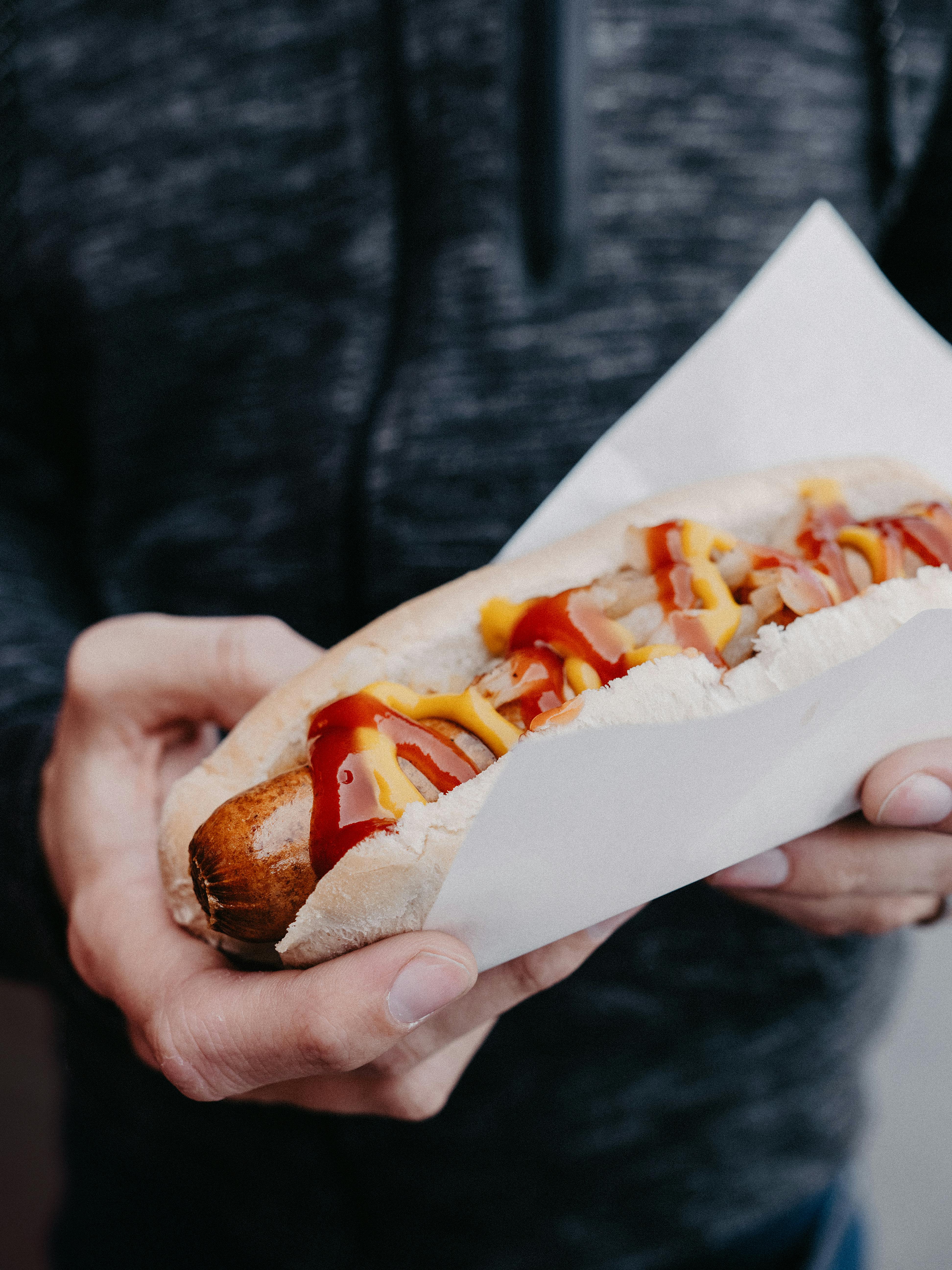 Enjoy a freshly prepared hot dog topped with mustard and ketchup, held in a white napkin.