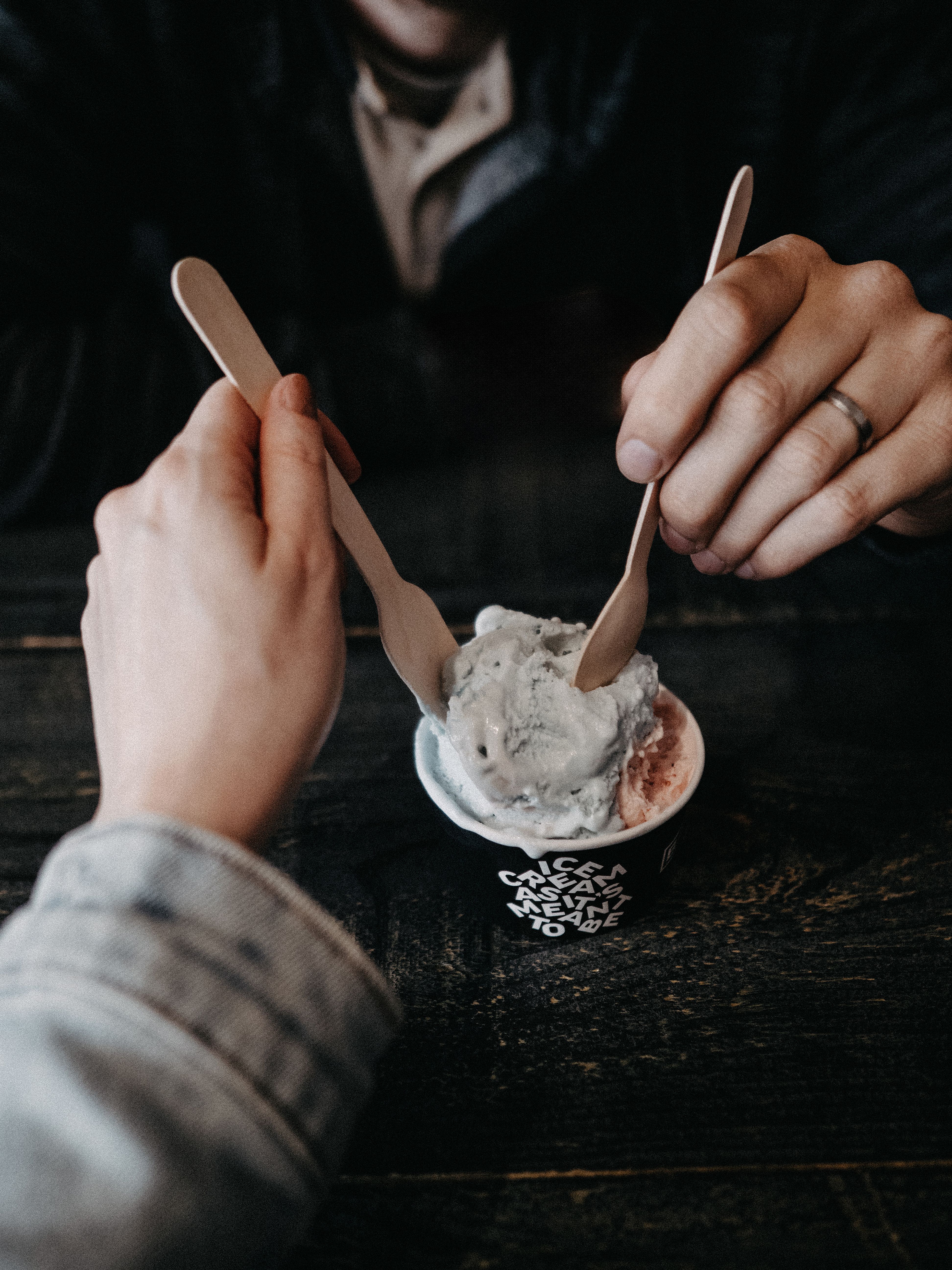 Fotomural Dos personas disfrutando de helado juntas, usando cucharas de madera en una cafetería.