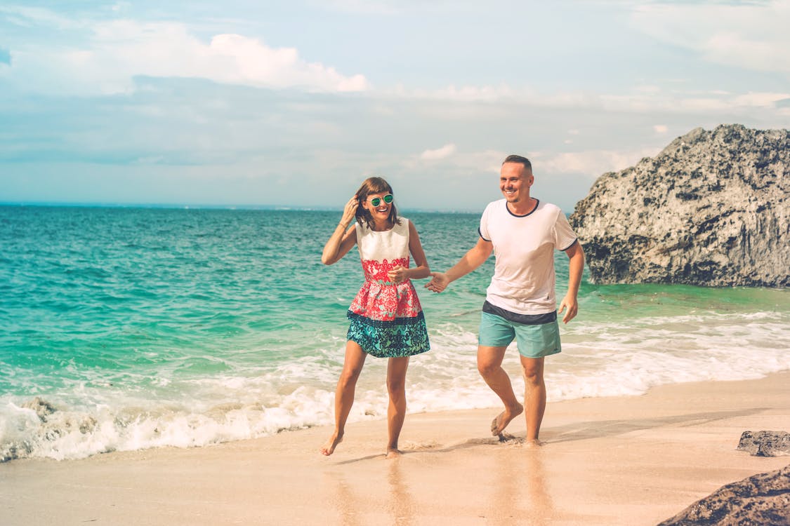 Photo of Laughing Couple Walking by the Beach