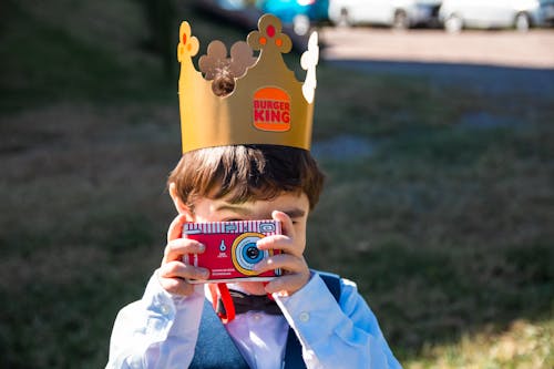 A boy wearing a crown taking a photo with a camera