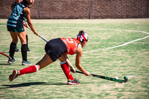 A woman in a red and black uniform playing field hockey