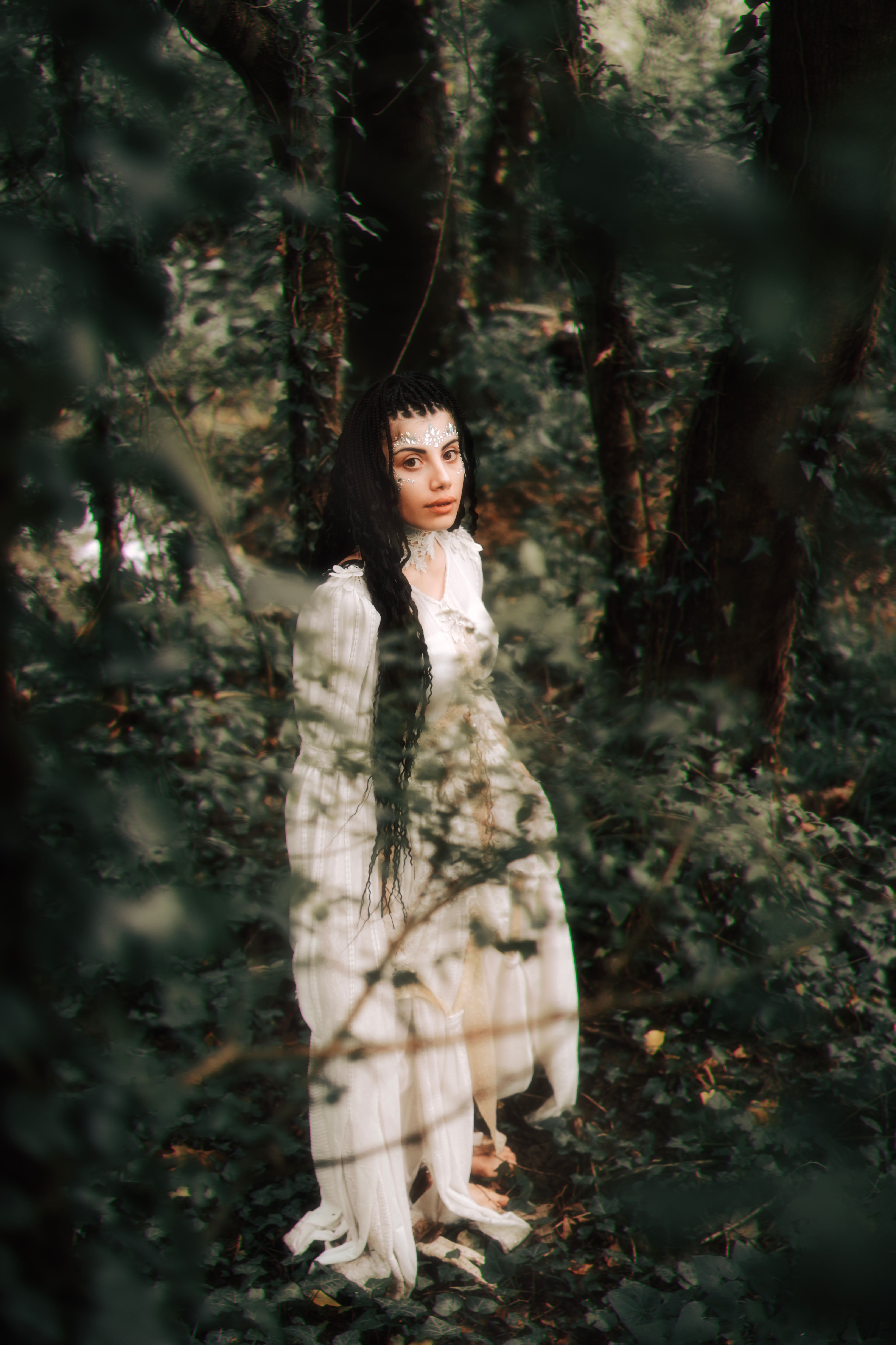 A woman in a flowing white dress stands in a mystical forest, exuding a serene and ethereal presence.