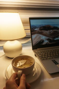 A warm, inviting workspace featuring a tea cup, laptop, and lamp for a relaxing work session.