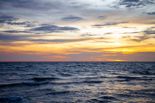 Free Serene ocean landscape with vibrant sunset and gentle waves under a cloudy sky. Stock Photo