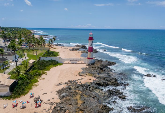 Aerial shot of Itapuã Lighthouse on a sunny beach in Salvador, Brazil, with waves crashing on the rocks.