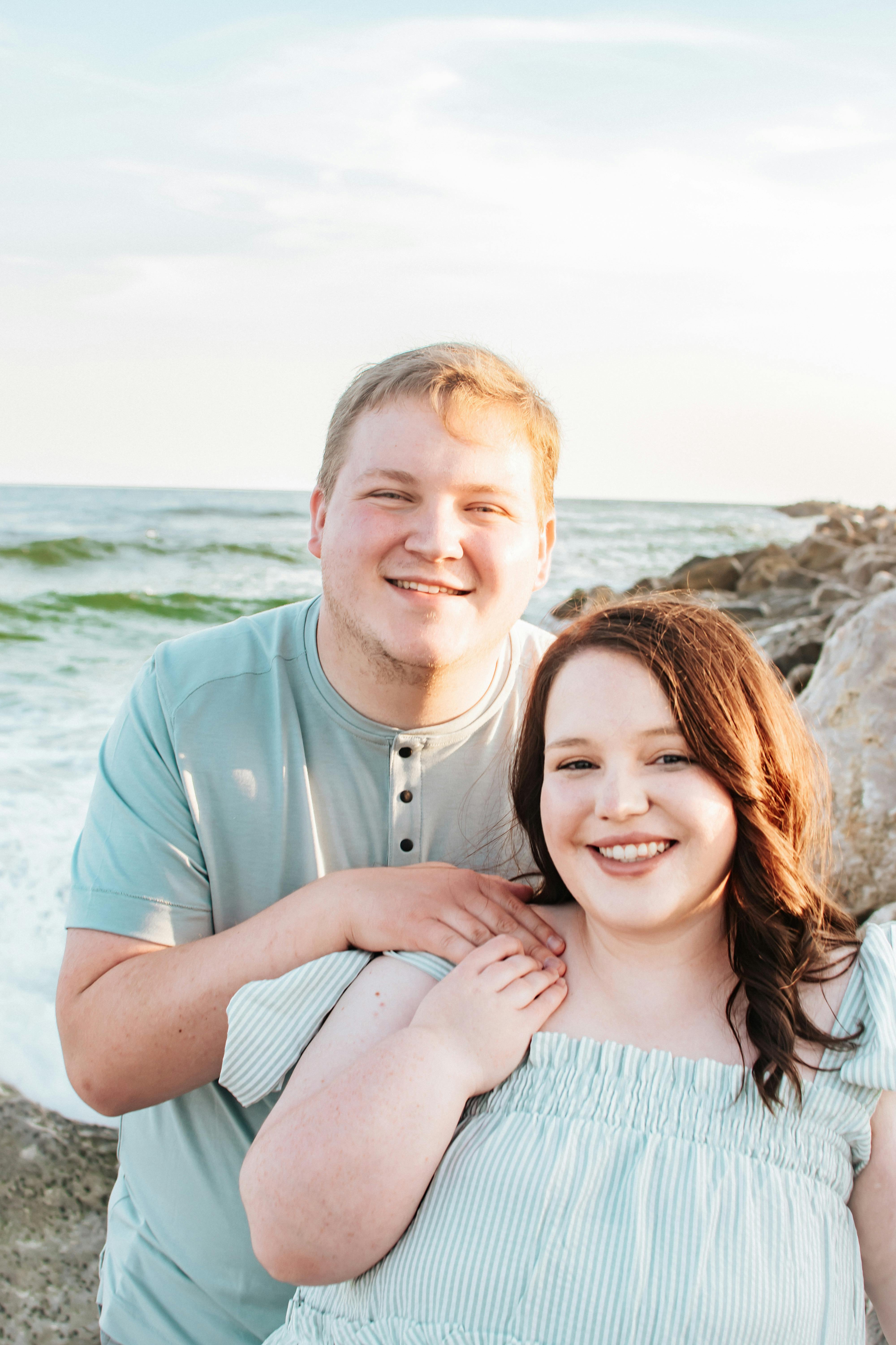 Joyful couple smiling and embracing by the beach during a beautiful sunset.