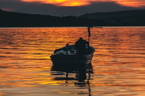 A man is sitting in a boat at sunset