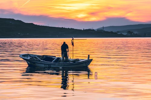 A man is standing in a small boat at sunset