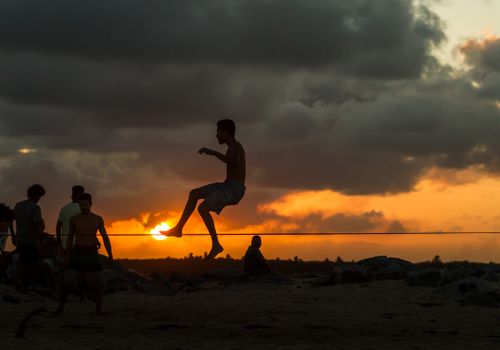 Dynamic silhouette of a man performing slacklining at sunset on a Brazilian beach with scenic golden skies.