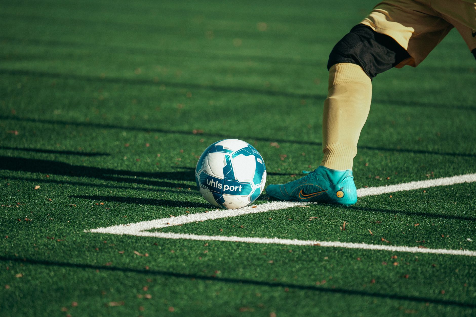 Close-up of a football player preparing to kick a blue and white soccer ball on a turf field.