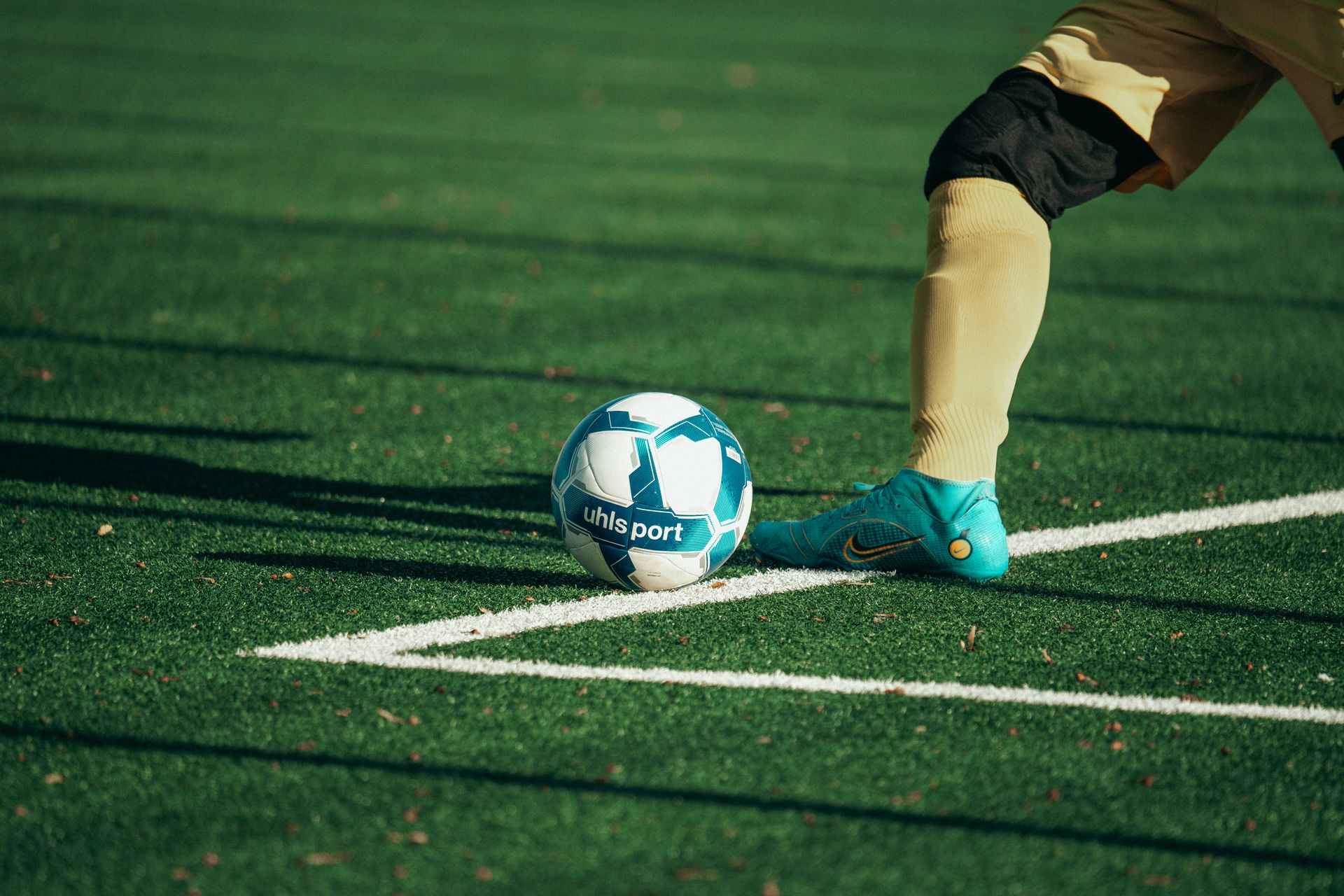 Close-up of a football player preparing to kick a blue and white soccer ball on a turf field.