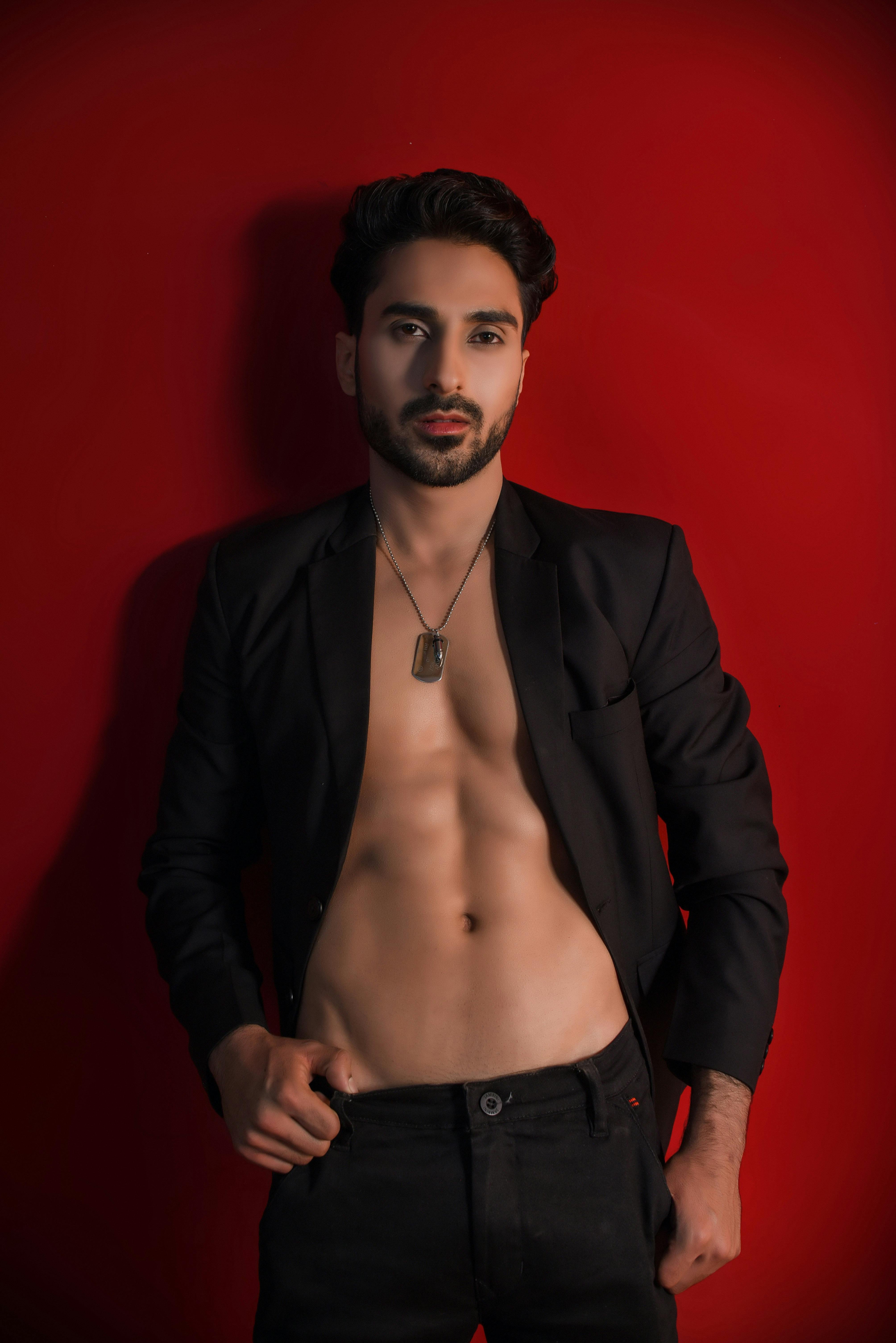 Shirtless man in blazer posing confidently against a vibrant red wall.