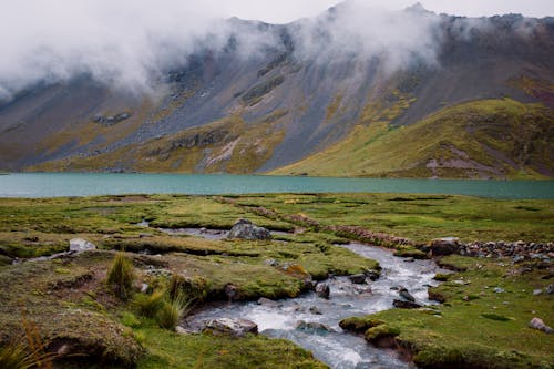 Free A stream runs through a grassy field next to a mountain Stock Photo