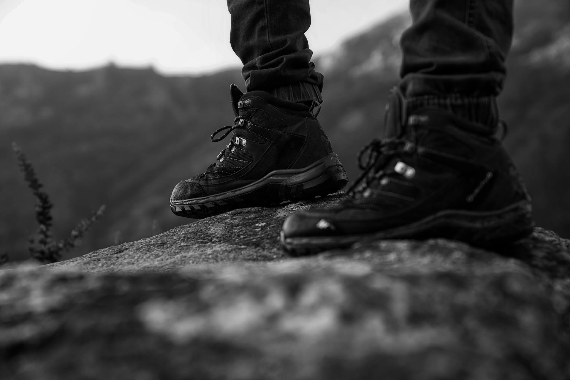 Close-up of hiking boots standing on a rock, showcasing outdoor adventure style in monochrome.