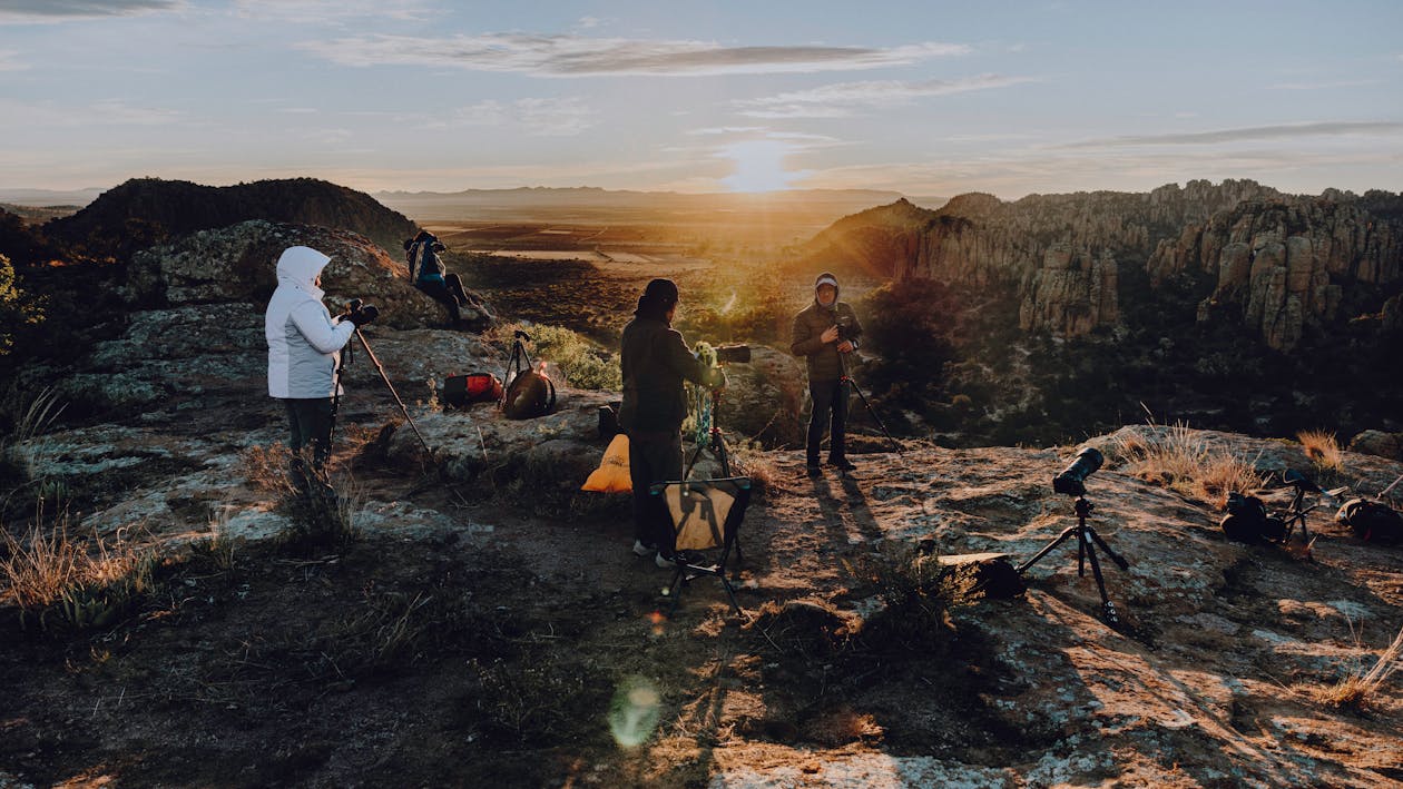A group of people standing on a mountain with the sun setting behind them