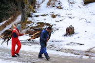 两名身着冬装的男子在白雪皑皑的风景中搬运柴火，展现了坚韧与团队合作的精神