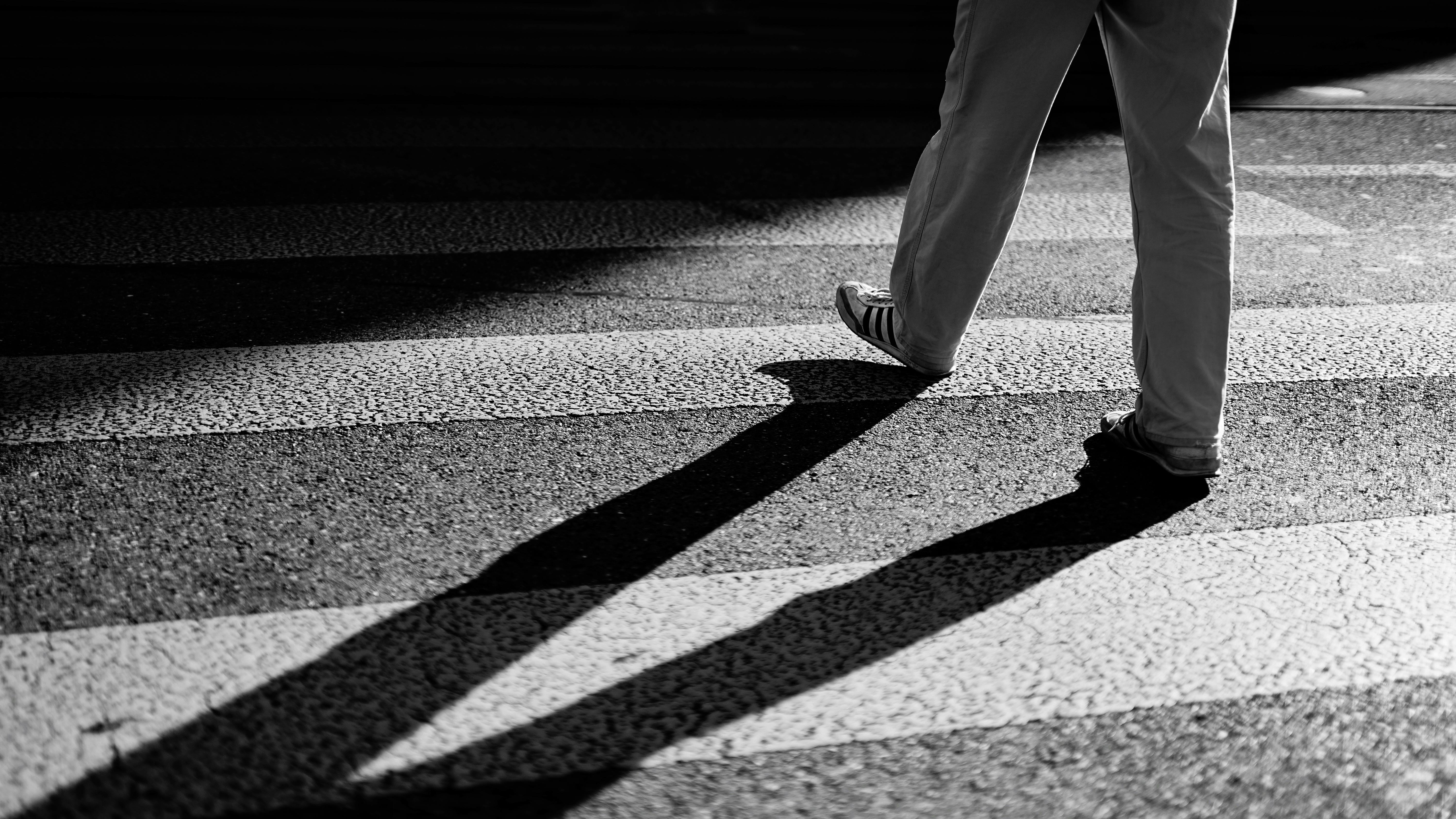 A person walking on a crosswalk casting a shadow in black and white.