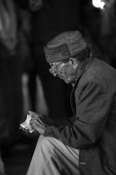 Black and white portrait of a reflective elderly man sitting and holding money.