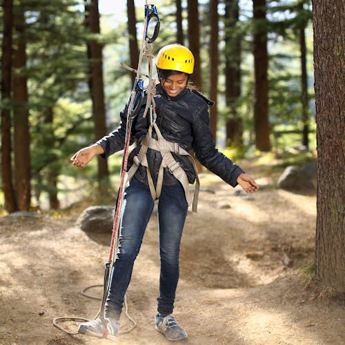 Woman Standing and Smiling While Putting Right Leg on Camping Rope Near Trees