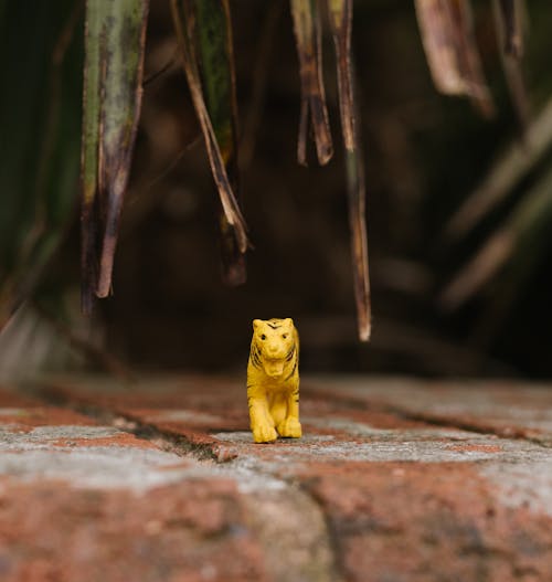 A yellow toy tiger is standing on a brick wall