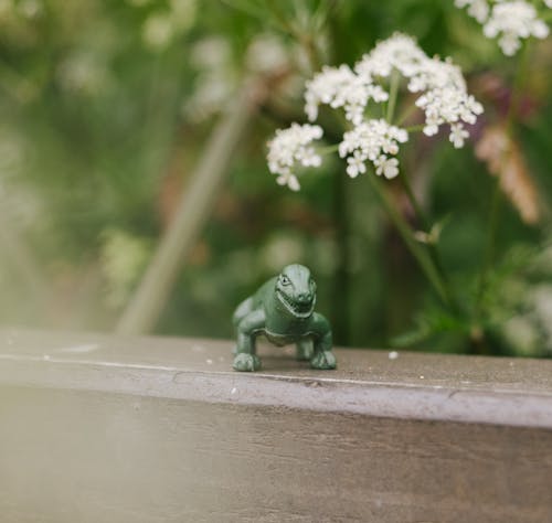 A toy dinosaur is sitting on a wooden fence