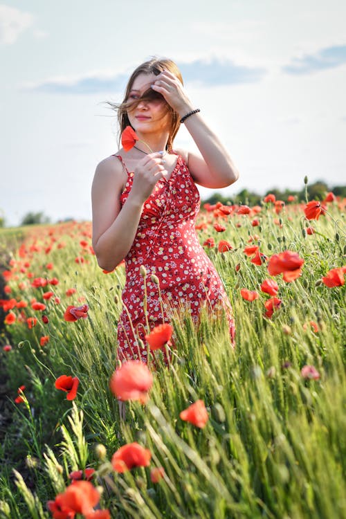 A woman in a red dress is standing in a field of poppies