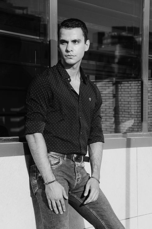 Free Stylish black and white portrait of a man in a polka dot shirt and jeans leaning against a wall. Stock Photo