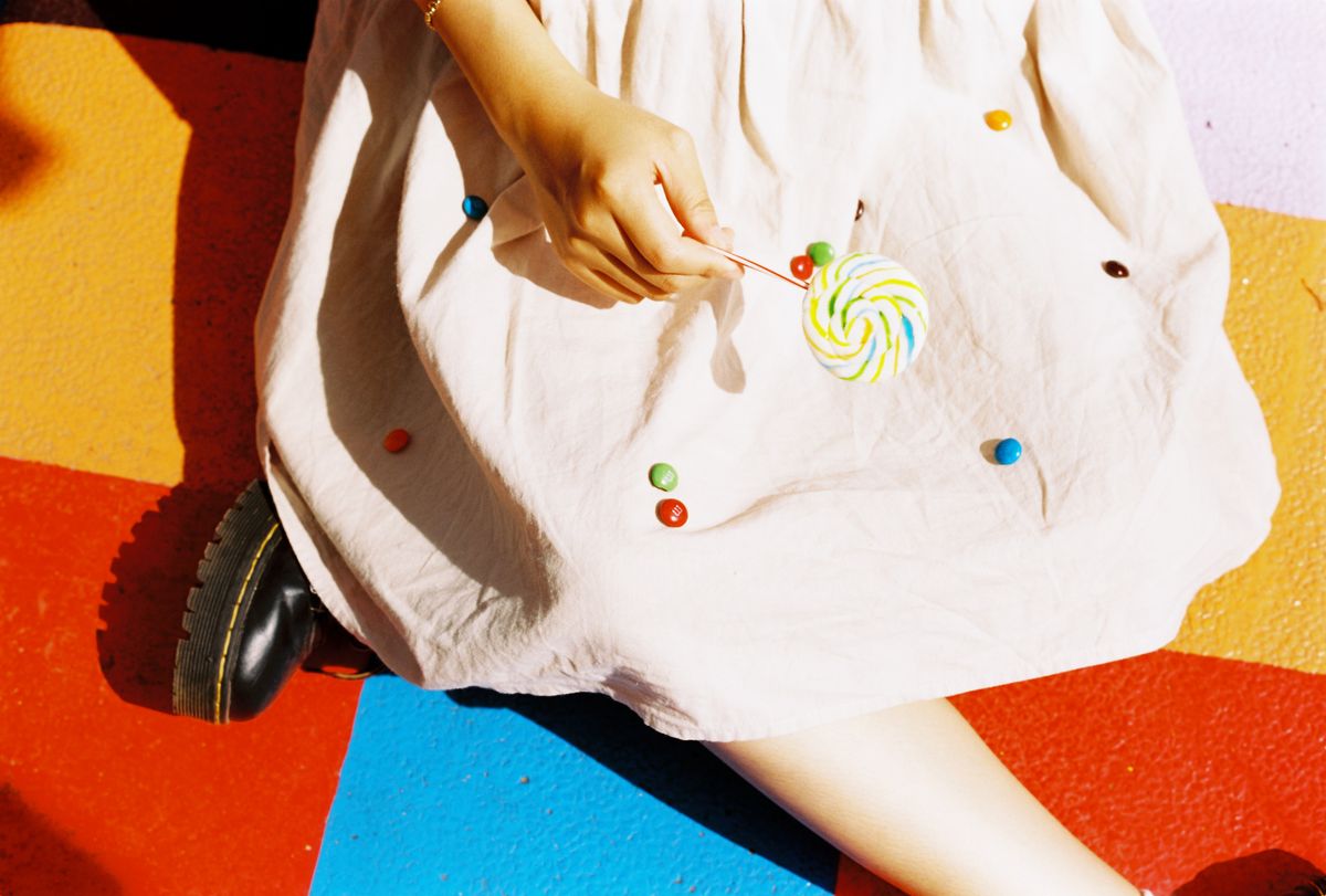A person holding a lollipop with candies on a colorful surface. Fun and playful vibe.